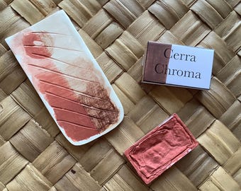May include: Three watercolor paint pans, one with a white and red striped design, one with a solid red color, and one with a brown label that reads "Cerra Chroma".