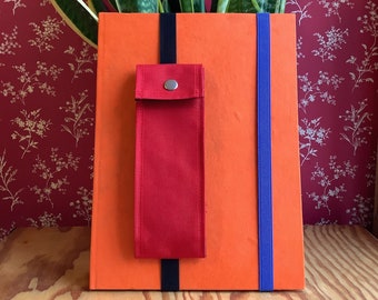 May include: A bright orange planter with a red fabric pocket and black and blue straps. The planter is filled with a green snake plant.