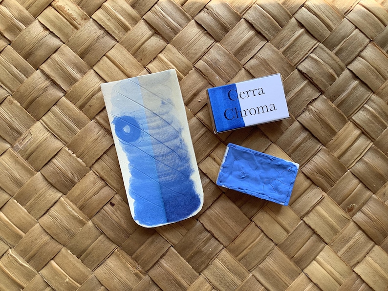 May include: A blue watercolor pan with the text "Cerra Chroma" on the packaging. The pan is sitting on a woven mat.