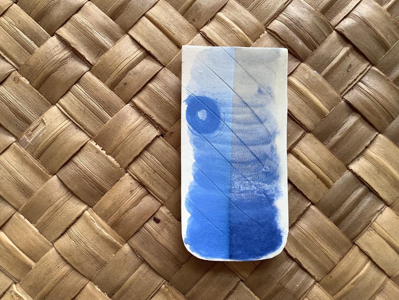 May include: A rectangular ceramic tile with a blue and white watercolor design. The tile has a textured surface and a slightly raised edge.