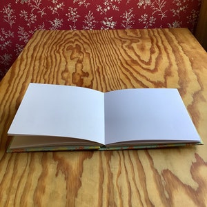 Puede incluir: Un libro blanco abierto, en blanco, con una cubierta con estampado azul claro y naranja sobre una mesa de madera.