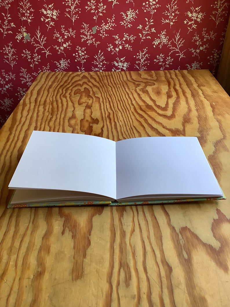 Puede incluir: Un libro blanco abierto, en blanco, con una cubierta con estampado azul claro y naranja sobre una mesa de madera.