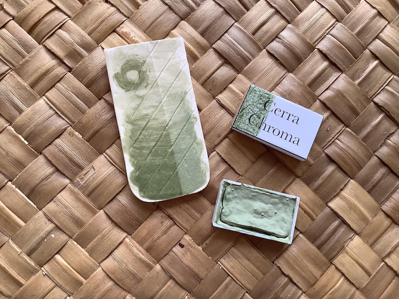May include: A green watercolor paint pan with the brand name "Cerra Chroma" on the packaging. The paint pan is sitting on a woven surface.