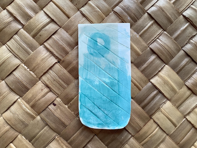 Pu&ograve; includere: Un dipinto ad acquerello blu chiaro su carta con sfondo bianco. Il dipinto presenta un motivo di linee diagonali e un cerchio al centro.