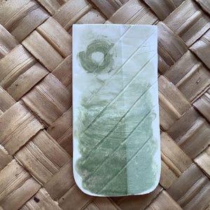 May include: A rectangular ceramic tile with a green and white glaze. The glaze has a swirling pattern and a light green color.