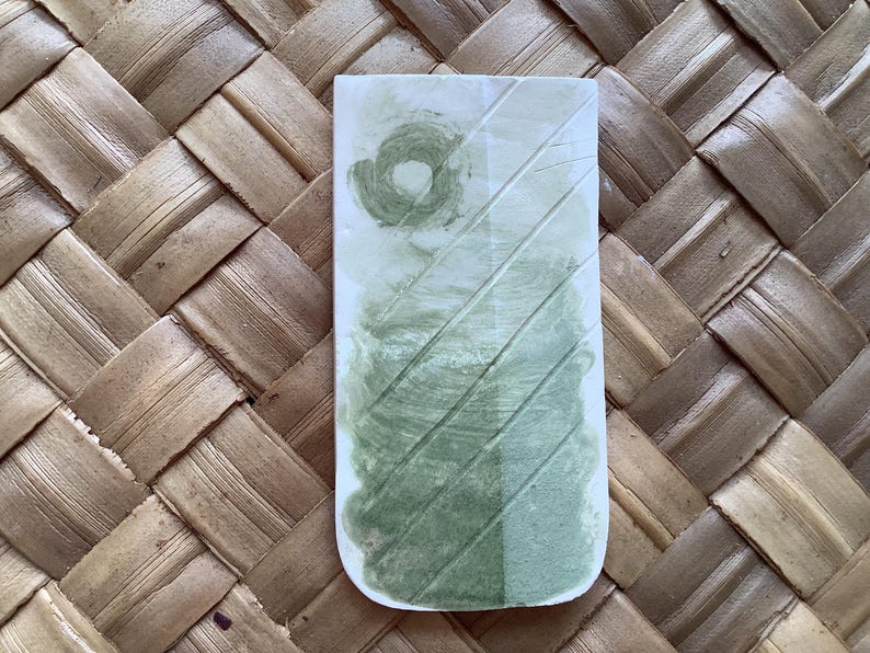 May include: A rectangular ceramic tile with a green and white glaze. The glaze has a swirling pattern and a light green color.