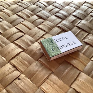 May include: A small, white box with green and black lettering that reads "Cerra Chroma Fire Iron Wine 06-10". The box is sitting on a woven, light brown surface.