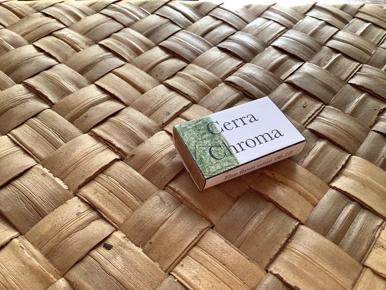 May include: A small, white box with green and black lettering that reads "Cerra Chroma Fire Iron Wine 06-10". The box is sitting on a woven, light brown surface.