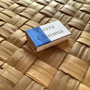 May include: A small white box with blue accents. The box has the text "Cerra Chroma" and "Fire from cone 06-10" printed on it.