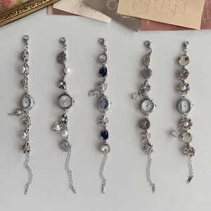 May include: Five silver charm bracelets, each with a small watch face. The bracelets are adorned with various charms such as pearls, hearts, flowers, and crystals. The watch faces have white dials and delicate hands.