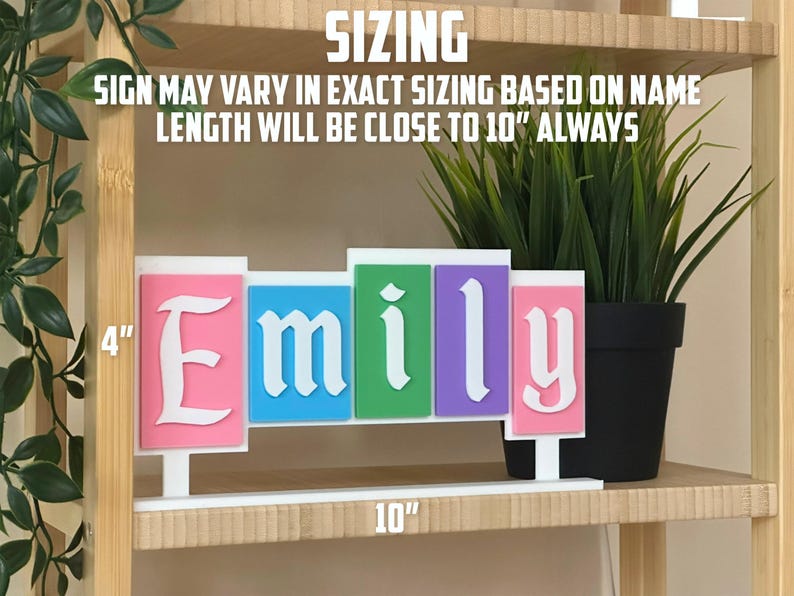 May include: A colourful custom name sign spelling "Emily" in white, with each letter on a different coloured background: pink, blue, green, and purple. The sign is approximately 25 cm long and 10 cm tall. The text "SIZING" is at the top.