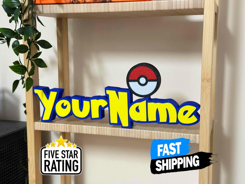 May include: A personalised sign featuring the text "Your Name" in yellow with a blue border, and a red, white, and black Pokeball design. The sign is displayed on a wooden shelf. A "Five Star Rating" and "Fast Shipping" sticker are also visible.