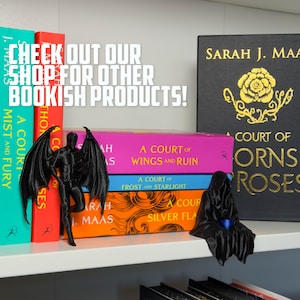May include: A shelf displays colorful books and black figurines. The books have titles like "A Court of Wings and Ruin" and "A Court of Thorns and Roses." The text "CHECK OUT OUR SHOP FOR OTHER BOOKISH PRODUCTS!" is visible.