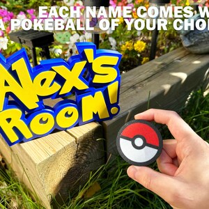 May include: A blue and yellow "Alex's Room" sign with a matching Pokeball. The sign is 3D and sits on a wooden surface. The text "EACH NAME COMES WITH A POKE BALL OF YOUR CHOICE!" is above the sign.