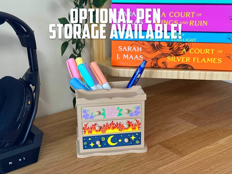 May include: A decorative wooden pen holder with three drawers, featuring floral, flame, and celestial designs. The text "OPTIONAL PEN STORAGE AVAILABLE!" is displayed above. The holder contains colourful pens and a blue pen.