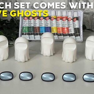 May include: Five white ghost-shaped figurines with black eyes and a black mouth. The figurines are arranged in a row on a white surface. There are ten tubes of acrylic paint in the background. The text "EACH SET COMES WITH FIVE GHOSTS" is visible at the top of the image.