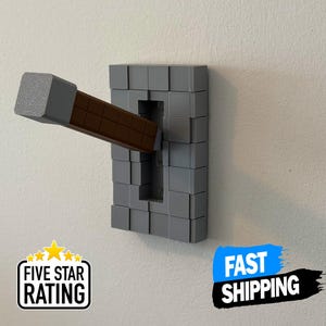 Op de afbeelding: Een grijze en bruine Minecraft-lichtschakelaar met een hendel in de neerwaartse stand. De schakelaar is gemaakt van kleine vierkante blokken.