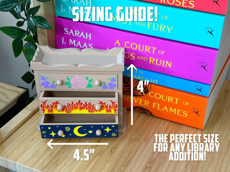 May include: A small, beige wooden drawer set with three drawers, each decorated with different designs. The top drawer has purple flowers and a pink rose, the middle drawer has flames, and the bottom drawer has a moon and stars. The set is 11.4 cm wide and 10.2 cm tall.