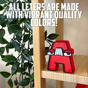 May include: A red letter A with white eyes and a black outline. The letter is made of a 3D printed material and is sitting on a wooden shelf. The text "ALL LETERS ARE MADE WITH VIBRANT QUALITY COLORS!" is visible in the background.