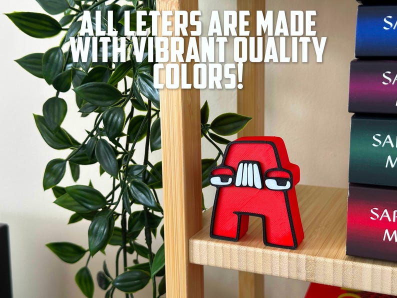 May include: A red letter A with white eyes and a black outline. The letter is made of a 3D printed material and is sitting on a wooden shelf. The text "ALL LETERS ARE MADE WITH VIBRANT QUALITY COLORS!" is visible in the background.