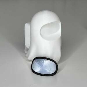 May include: A white 3D printed ghost figure with a black visor. The ghost is standing on a white surface.