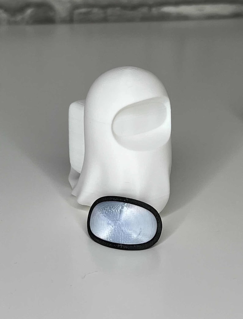 May include: A white 3D printed ghost figure with a black visor. The ghost is standing on a white surface.