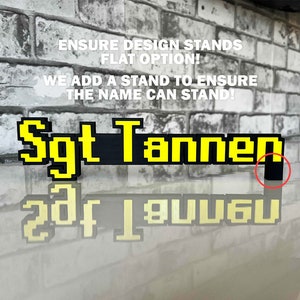 May include: A black and yellow pixelated name sign that reads "Sgt Tannen". The sign is made to stand up on a small black stand.