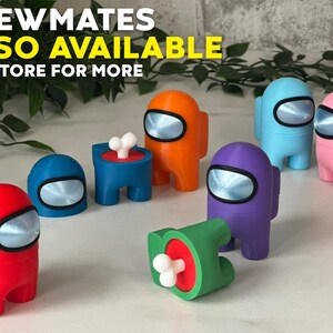 Puede incluir: Un conjunto de figuras de personajes de Among Us de colores, que incluyen rojo, azul, naranja, morado, rosa y verde. Las figuras est&aacute;n hechas de pl&aacute;stico y tienen un aspecto de impresi&oacute;n 3D. El texto "CREWMATES ALSO AVAILABLE SEE STORE FOR MORE" es visible en la imagen.