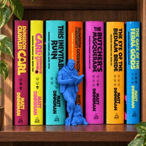 Könnte beinhalten: Eine Reihe von sechs bunten Büchern von Matt Dinniman mit den Titeln Dungeon Crawler Carl, Carl's Doomsday Scenario, This Inevitable Ruin, Dungeon Crawler Carl's Cookbook, The Butcher's Masquerade, The Eye of the Bedlam Bride und The Gate of the Feral Gods.