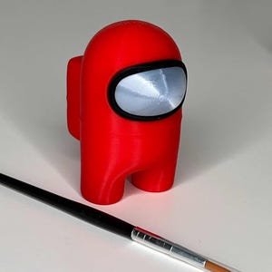 K&ouml;nnte beinhalten: Eine rot 3D-gedruckte Figur eines Charakters aus dem Videospiel Among Us. Der Charakter hat ein schwarzes Visier und steht auf einer wei&szlig;en Oberfl&auml;che.