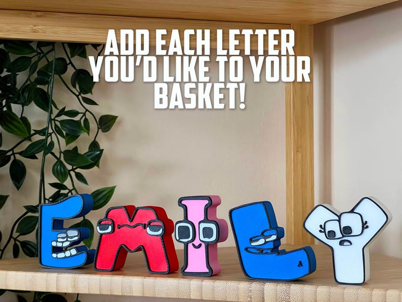 May include: Wooden letters spelling "EMILY" in blue, red, and pink, with cartoon-like faces. The text above reads "ADD EACH LETTER YOU'D LIKE TO YOUR BASKET!" on a wooden shelf.