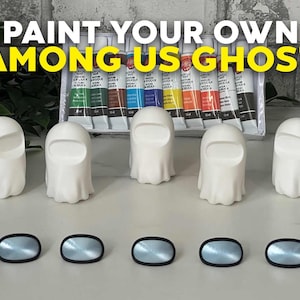May include: Five white ceramic ghost figurines with black eye holes, ready to be painted. The ghosts are arranged in a row on a gray surface. A set of acrylic paints is visible in the background. The text "PAINT YOUR OWN AMONG US GHOST" is displayed at the top of the image.