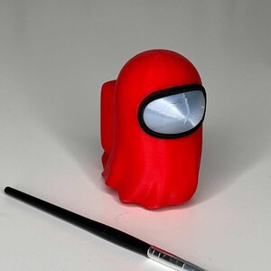 May include: A red 3D printed figurine of a character from the popular video game Among Us. The figurine is in the shape of a crewmate with a large, round head and a small body. The crewmate is wearing a red spacesuit with a black visor.