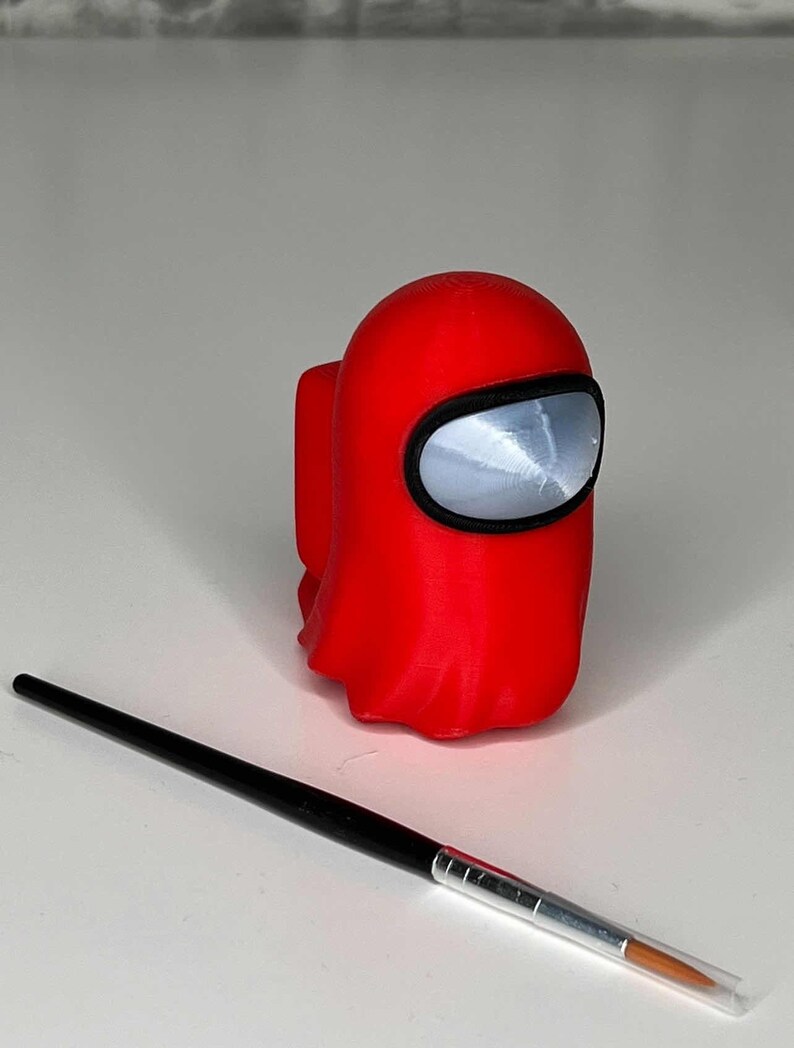May include: A red 3D printed figurine of a character from the popular video game Among Us. The figurine is in the shape of a crewmate with a large, round head and a small body. The crewmate is wearing a red spacesuit with a black visor.