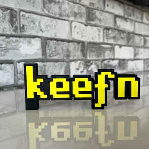 May include: A black and yellow pixelated sign that reads "keefn".
