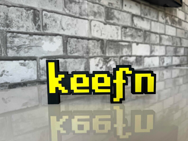 May include: A black and yellow pixelated sign that reads "keefn".