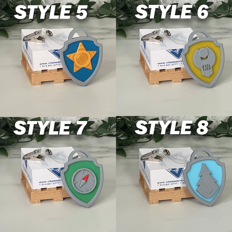 May include: Four different styles of Paw Patrol character badge keychains. Each keychain features a different character's badge with a gray, plastic backing. The badges are yellow, blue, green, and light blue. The keychains are displayed on small wooden crates.