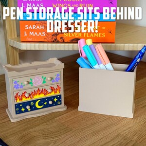 May include: A beige wooden pen holder and a decorative dresser-shaped pen storage box. The dresser has floral, flame, and celestial designs. The text "PEN STORAGE SITS BEHIND DRESSER!" is visible above the items.