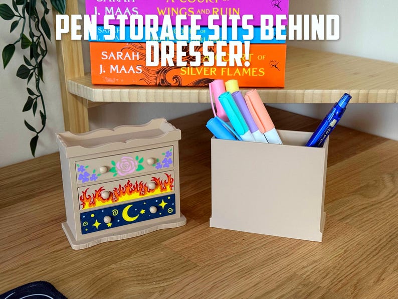 May include: A beige wooden pen holder and a decorative dresser-shaped pen storage box. The dresser has floral, flame, and celestial designs. The text "PEN STORAGE SITS BEHIND DRESSER!" is visible above the items.