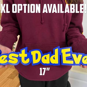 May include: A blue and yellow sign reading "Best Dad Ever" in a stylized font. The sign is 43 cm long and 10 cm tall. The text "XL OPTION AVAILABLE!" is above the sign.