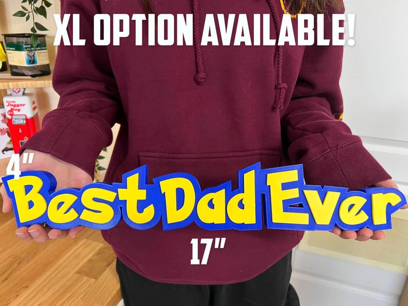 May include: A blue and yellow sign reading "Best Dad Ever" in a stylized font. The sign is 43 cm long and 10 cm tall. The text "XL OPTION AVAILABLE!" is above the sign.