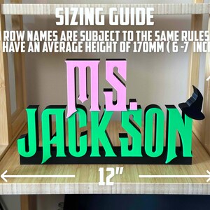 May include: A green and pink wooden sign with the text "MS. JACKSON" and a witch's hat. The sign is 12 inches wide and 7 inches tall.