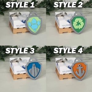 May include: Four different styles of gray plastic badge holders with various colored icons. The icons include a paw print, a recycling symbol, a building, and an anchor. Each badge holder has a clear plastic strap and a metal clip.