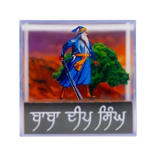 May include: A blue and yellow religious figure holding a sword, standing in front of a tree with a sunset background. The text "ਖ਼ਾਲਸਾ ਦੀ ਸ਼ਕਤੀ" is written in black on a gray background.