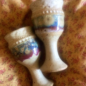 May include: Two ceramic goblets with speckled brown glaze and blue and purple accents. The goblets have a white rim and a band of raised dots around the top.