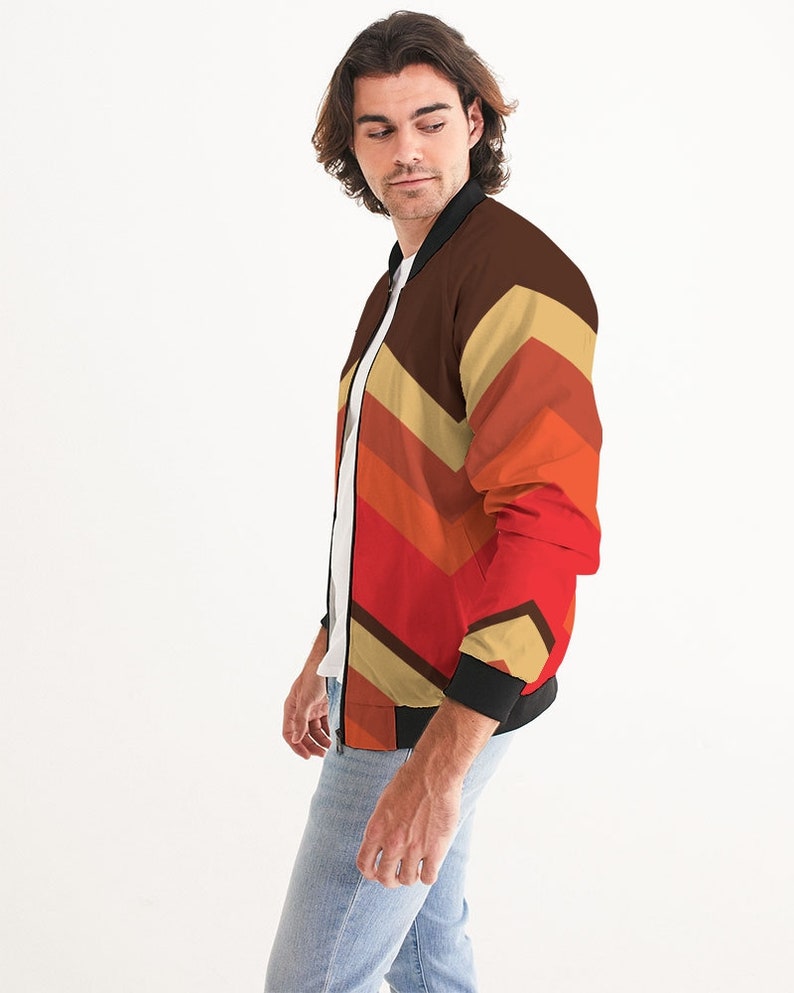 May include: A bomber jacket with a geometric pattern in shades of brown, orange, red, and beige. The jacket has a black zipper and black ribbed cuffs and collar.
