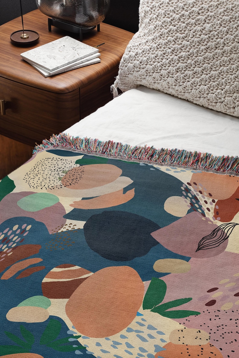 May include: A colorful throw blanket with a geometric pattern of abstract shapes in shades of blue, green, pink, and orange. The blanket has a fringed edge.