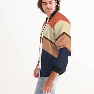 Op de afbeelding: Een marineblauwe bomberjack met een geometrisch patroon in tinten oranje, bruin en beige.