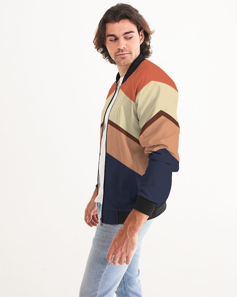 Op de afbeelding: Een marineblauwe bomberjack met een geometrisch patroon in tinten oranje, bruin en beige.