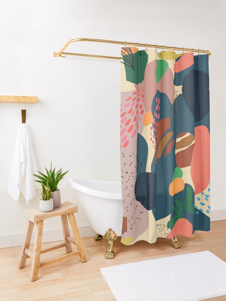 May include: A colorful shower curtain with an abstract design. The curtain features large shapes in shades of blue, pink, orange, and green against a cream background. The curtain hangs from a gold-colored rod in a bathroom setting.